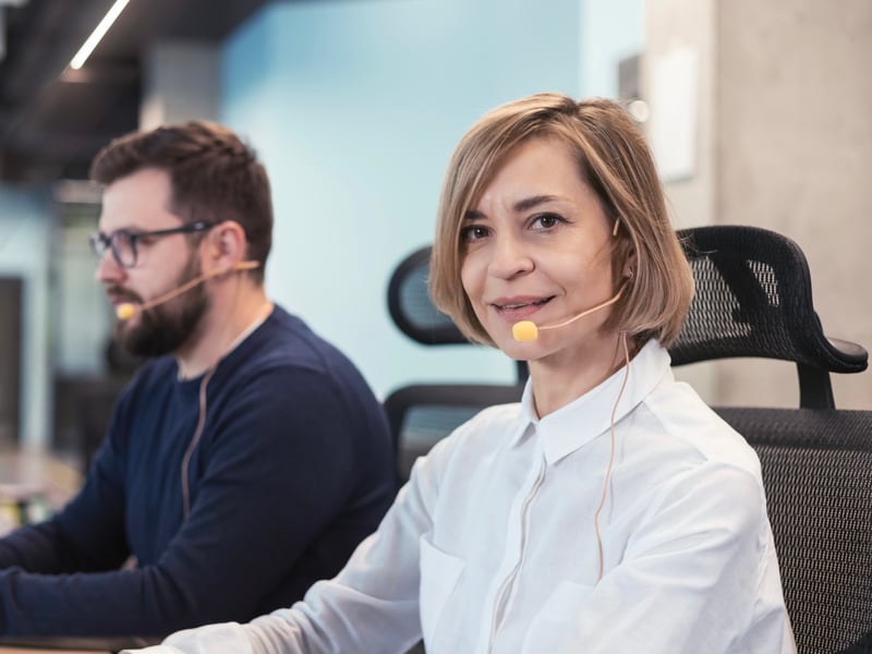 Eine Frau und ein Mann telefonieren mit Headset an ihren Arbeitsplätzen im Büro